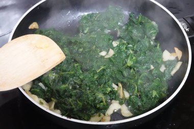 Isırgan otları ve sarımsak karanfilleri, ahşap bir spatulayla kızartma tavasında pişiriliyor.