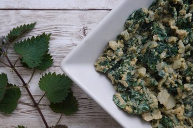 Çırpılmış yumurta ve taze koparılmış ısırgan otları beyaz bir kasede beyaz tahta bir masada servis edilir, sağlıklı ve lezzetli bir kahvaltı hazırlar.