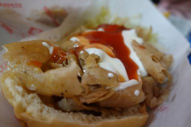 Et, kremalı beyaz sos ve kızarmış ekmeğin içine yerleştirilmiş canlı kırmızı sosla dolup taşan bir kebabın yakın çekimi, tadını çıkarmaya hazır.