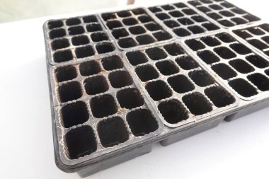 Boş siyah plastik fidan tepsisi önceki ekim mevsimlerinden kalan toprak ve aşınmaları gösteriyor, şimdi yeni tohumlara hazır.