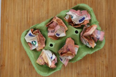 Buruşmuş avro banknotları yeşil bir yumurta kutusunda duruyor ve gıda maliyetlerinin artması ve enflasyonun tüketici harcamaları üzerindeki etkisini vurguluyor.