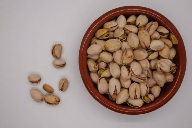 Kavrulmuş şam fıstıkları küçük bir terracotta kasesinden temiz beyaz bir arka plana dökülüyor ve görsel olarak çekici bir düzenleme yaratıyor.