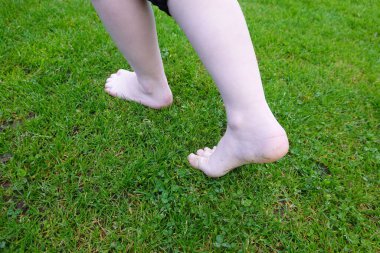 Çocuk yemyeşil çimenlerde yalınayak yürüyor, kaygısız bir sevinç anında küçük ayakların altındaki yumuşak çimlerin zevkini çıkarıyor.