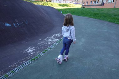 Parkta paten yapan genç bir kız güneşli bir günün tadını çıkarırken dışarıda eğleniyor ve özgürce eğleniyor.