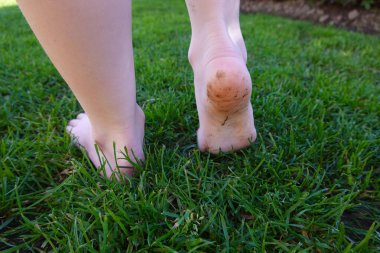 Yalın ayaklı çocuk yemyeşil çimenlerde neşeyle yürüyor, canlı bir bahçede doğanın güzelliğini kucaklıyor, tasasız ve mutlu hissediyor.