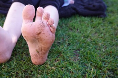 Açık hava oyununun, kaygısız yaz eğlencesinin ve özgürlüğün vücut bulmuş halinin tadını çıkardıktan sonra yemyeşil çimlerde dinlenen bir çocuğun kirli çıplak ayakları.