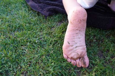 Kirli, çıplak ayaklı bir çocuğu çimlerin üzerinde bir battaniyede otururken görmek, dışarıda kaygısız bir yaz gününün tadını çıkarmak.