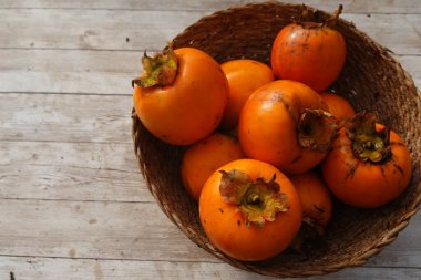 Dokuma sepetine yerleştirilmiş canlı portakal hurmaları kırsal ahşap sehpaya sonbahar sıcaklığını getirir.