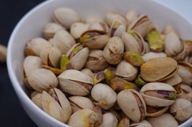Açık kabuklu kavrulmuş şam fıstığı. İçindeki yeşil fındıkları ortaya çıkarıyor. Arka plandaki beyaz kaseyi dolduruyor.