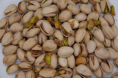 Çerçeveyi dolduran kavrulmuş şam fıstıkları açık deniz kabukları ve yeşil tohumlardan oluşan dokulu bir zemin oluşturuyor.