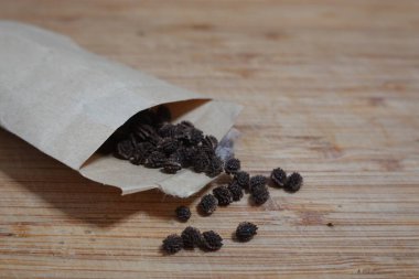 Kurumuş papaya tohumları küçük kahverengi kağıt zarflardan ahşap masaya dökülüyor, ekime ya da tüketime hazır.