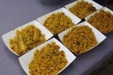 Safran paella pilavı, bezelye, sebze ve et dolu karton tepsiler, bir sokak yiyecek pazarında servis edilmeye hazır.
