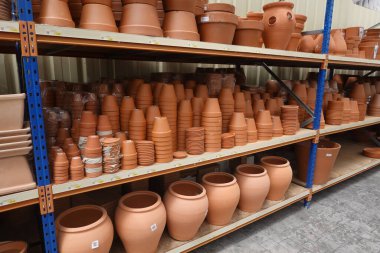 Çeşitli boyutlarda çok sayıda terracotta saksısı bir bahçe merkezindeki raflarda düzgünce istiflenmiş, satılmaya hazır.