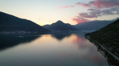 Perast 'in 4k hava görüntüsü, Montgro' nun ünlü turistik kasabalarından biri, gün batımında, renkli bulutlar denizi yansıtıyor.