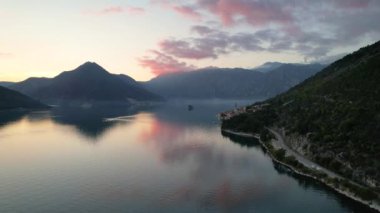 Perast 'in 4k hava görüntüsü, Montgro' nun ünlü turistik kasabalarından biri, gün batımında, renkli bulutlar denizi yansıtıyor.