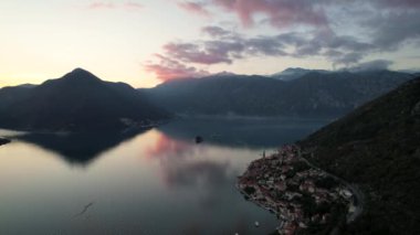 Perast 'in 4k hava görüntüsü, Montgro' nun ünlü turistik kasabalarından biri, gün batımında, renkli bulutlar denizi yansıtıyor.