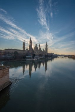 Zaragoza 'nın önemli mimari sembollerinden biri olan del Pilar Bazilikası ve Ebro nehri ve günbatımı renkleri ve bulutlarıyla yansıması.