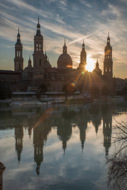 Zaragoza 'nın önemli mimari sembollerinden biri olan del Pilar Bazilikası ve Ebro nehri ve günbatımı renkleri ve bulutlarıyla yansıması.