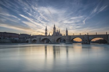 Zaragoza 'nın önemli mimari sembollerinden biri olan del Pilar Bazilikası ve Ebro nehri ve günbatımı renkleri ve bulutlarıyla yansıması.