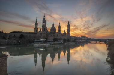 Zaragoza 'nın önemli mimari sembollerinden biri olan del Pilar Bazilikası ve Ebro nehri ve günbatımı renkleri ve bulutlarıyla yansıması.