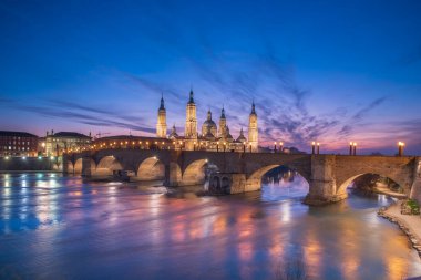Zaragoza 'nın önemli mimari sembollerinden biri olan del Pilar Bazilikası ve Ebro nehri ve günbatımı renkleri ve bulutlarıyla yansıması.