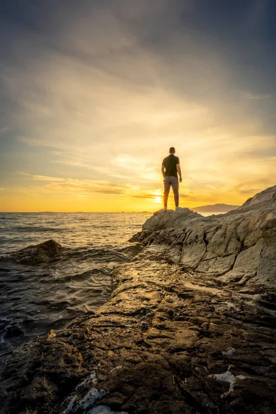 stock image Young man standing on rocky beach at sunset time  
