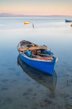 Günbatımında tekneler ve gökyüzü durgun suda yansıyor.