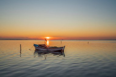 Günbatımında tekneler ve gökyüzü durgun suda yansıyor.