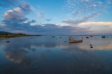 Günbatımında tekneler ve gökyüzü durgun suda yansıyor.