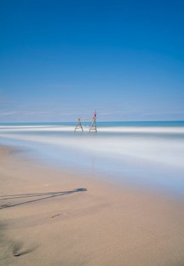 Ağaç dalları ve salıncaklar denizin arasında ve dalgalar mavi gökyüzüyle sahilde
