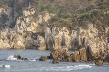 Sahilde deniz kenarında kayaların oluşturduğu renkli günbatımı fotoğrafları ve bir peçe gibi çekilen deniz.