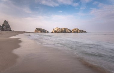 Sahilde deniz kenarında kayaların oluşturduğu renkli günbatımı fotoğrafları ve bir peçe gibi çekilen deniz.