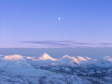 Norveç Lofoten Adaları ve Tromso arasındaki yol karla kaplı ve kar temizleme araçları çalışıyor ve günbatımı renkleri dağlara vuruyor.