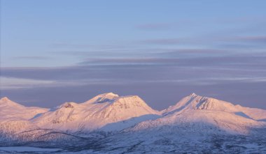 Norveç Lofoten Adaları ve Tromso arasındaki yol karla kaplı ve kar temizleme araçları çalışıyor ve günbatımı renkleri dağlara vuruyor.