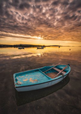 Yansıtıcı su bulutlarında gün batımı renklerinde tekneler bekliyor.