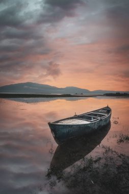 Yansıtıcı su bulutlarında gün batımı renklerinde tekneler bekliyor.
