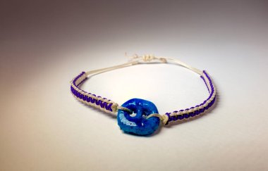 Beyaz arka planda mavi nazar boncuklarıyla örülmüş bilezik.