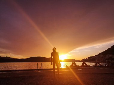 Elinde frizbi olan bir adam iskelede gün batımına doğru yürüyor.