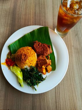 Bir tabak dolusu Nasi Rendang yemeği, tatlı buzlu çayla servis edilir ve Endonezya mutfağında lezzetli bir yemek deneyimi sunulur.