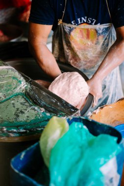 Bir adam pazarda kıyma makinesini ustalıkla çalıştırıyor. Köfte pişirme hizmetlerini istekli müşterilere sunuyor. Geleneksel mutfak işçiliğinin özünü somutlaştırıyor.