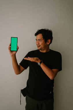 Adamın biri yeşil ekran bir telefonu tutup kameraya doğrultuyor.