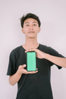 Elinde yeşil ekran telefon tutan Güneydoğu Asyalı bir adam. Özel içerik, uygulama arayüzleri veya pazarlama mesajları eklemek için mükemmel, çok yönlü bir bağlamda teknoloji kullanımı.