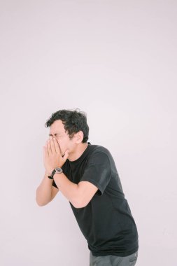 Burnunu tutarken hapşıran Güneydoğu Asyalı bir adam. Çeşitli pazarlama ve editoryal bağlamlarda sağlık, alerji veya soğuk semptomlara uygun bir rahatsızlık anı yakalar