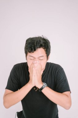 Burnunu tutarken hapşıran Güneydoğu Asyalı bir adam. Çeşitli pazarlama ve editoryal bağlamlarda sağlık, alerji veya soğuk semptomlara uygun bir rahatsızlık anı yakalar