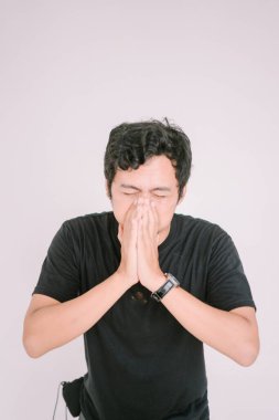 Burnunu tutarken hapşıran Güneydoğu Asyalı bir adam. Çeşitli pazarlama ve editoryal bağlamlarda sağlık, alerji veya soğuk semptomlara uygun bir rahatsızlık anı yakalar