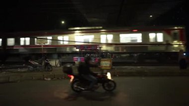 Bogor, 7 Haziran 2024. Geceleyin işlek bir cadde. Aracın farları ve sokak lambalarıyla aydınlatılıyor. Şehir gece hayatının dinamik parıltısını ve etkinliğini yakalıyor.