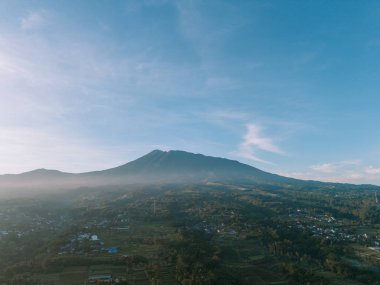 Aydınlık sisli ve parlak bulutlu Gede Dağı 'nın sabah manzarası dingin ve berrak güzelliği yakalıyor.