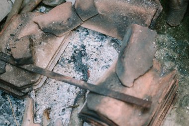 Yanmış kömür kalıntıları, kül ve kararmış parçalarla, bir yangının sonrasını vurguluyor.