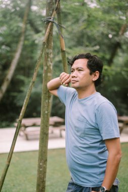 Asyalı bir adam ciddi bir ifadeyle ileriye bakarken yanağını tutuyor, derin bir düşünce ya da endişe anı yakalıyor.