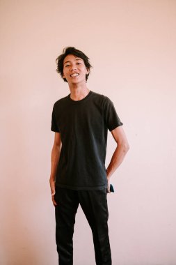 Güneydoğu Asyalı bir adam kameraya samimi ve davetkar bir görüntü oluşturarak gülümsüyor.